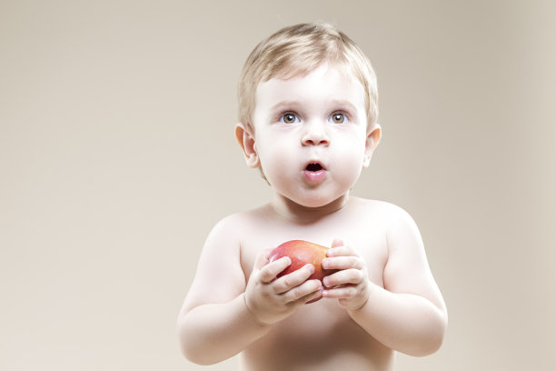 孩子的概念。在米色的背景下，一个拿着食物吃着红苹果的小孩的特写图片下载