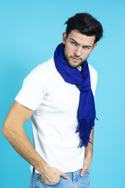 白种人帅哥穿着白色衬衫，戴着深蓝色围巾摆姿势，在蓝色背景下看着镜头图片下载