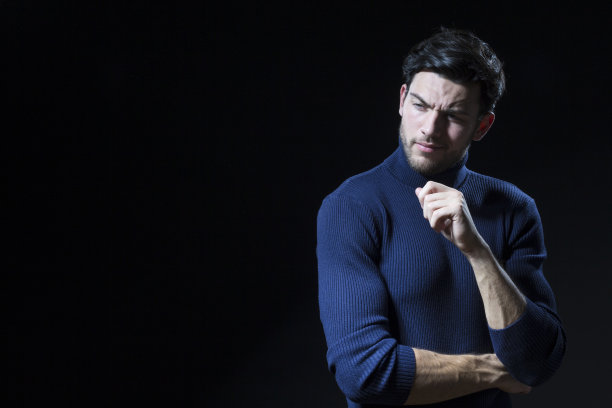 英俊的黑发男子在蓝色的海龟领毛衣摆姿势与黑色背景与复制空间作为成功的年轻人。图片下载