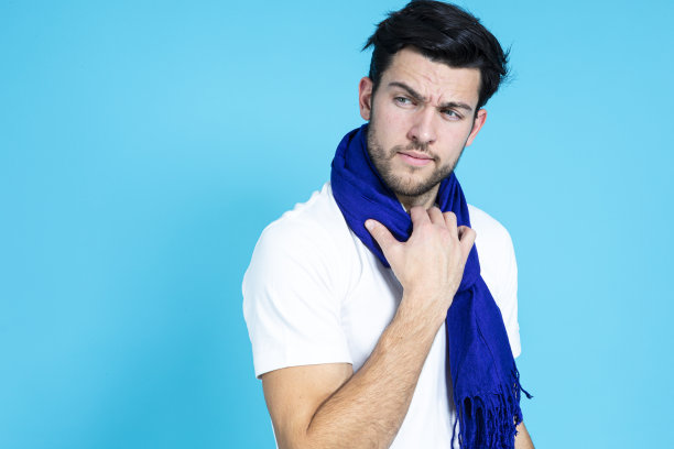 白种人帅哥穿着白色衬衫，戴着深蓝色围巾摆姿势，在蓝色的背景下看着一边图片下载