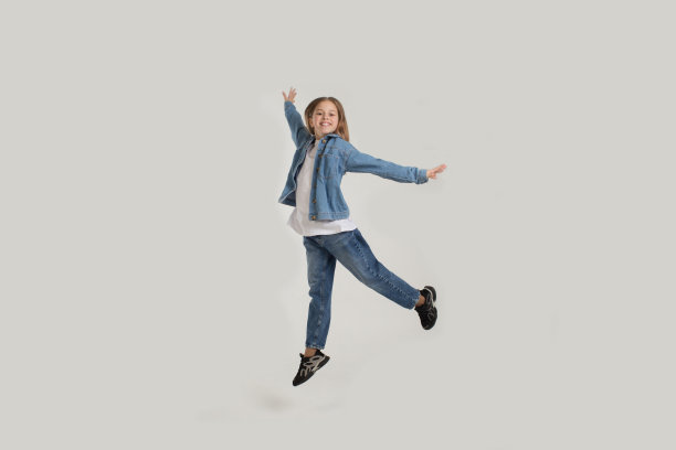 一个穿着牛仔裤的年轻女孩在白色的背景上快乐地跳跃着图片下载