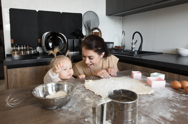 一位年轻的母亲带着一个小女儿正在厨房里愉快地做饭图片下载