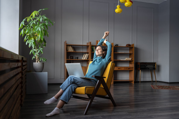 满意的女性自由职业者坐在椅子上与笔记本电脑放松，而远程工作在家图片下载