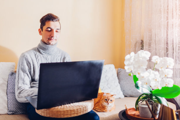 男人在家里用笔记本电脑和宠物在线工作。在冠状病毒封锁期间，自由职业者在电脑上打字图片下载