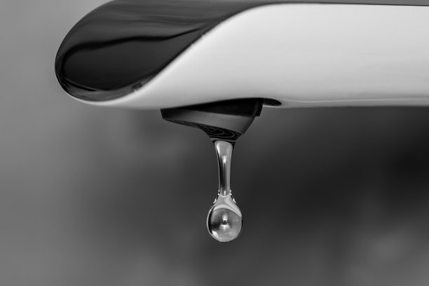 清澈的水从水龙头里滴下来。黑白摄影。图片下载