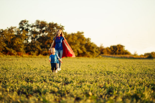 概念超级妈妈带着宝宝，妈妈穿着超级英雄斗篷在户外追着宝宝跑图片下载