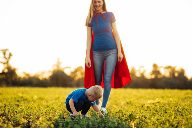 幸福的家庭，妈妈和她的小儿子穿着超级英雄的服装，在阳光明媚的日子里在户外种一棵树苗图片下载