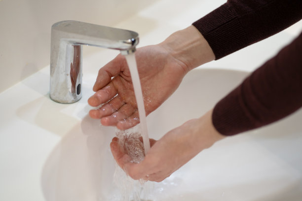 照片中，一名身穿毛衣的男子在白色水槽里的水里洗手。清洁和卫生图片下载