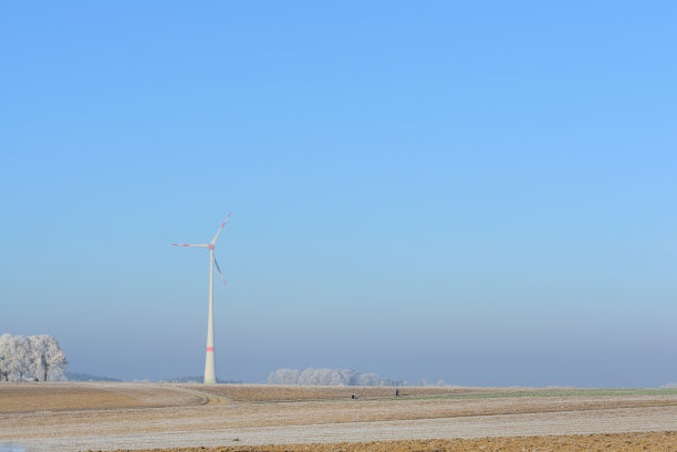 这张照片拍摄于巴伐利亚州的冬日，广阔的田野被霜冻覆盖，背景是蓝色的天空，还有一个用来发电的大型风车图片下载