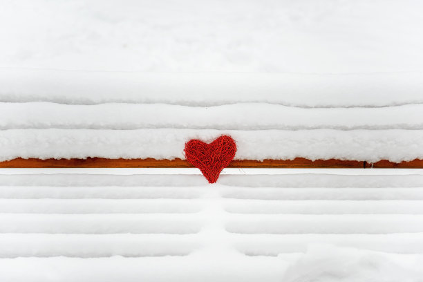 在一个木凳上躺着一颗红藤心在白雪的背景下的雪林。图片下载