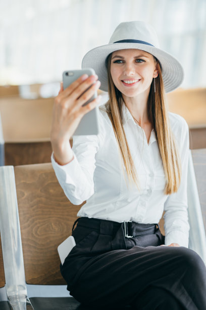 一个在机场候机楼打电话的女人。在一个阳光明媚的夏日，一位年轻的女性旅行者在公共交通站拿着行李、咖啡杯和手机图片下载