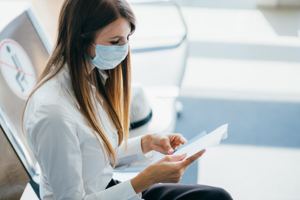 因新型冠状病毒感染症(covid - 19病毒)疫情，在候机楼候机大厅，一名女性戴着口罩，站在候机楼窗口等待出发图片下载