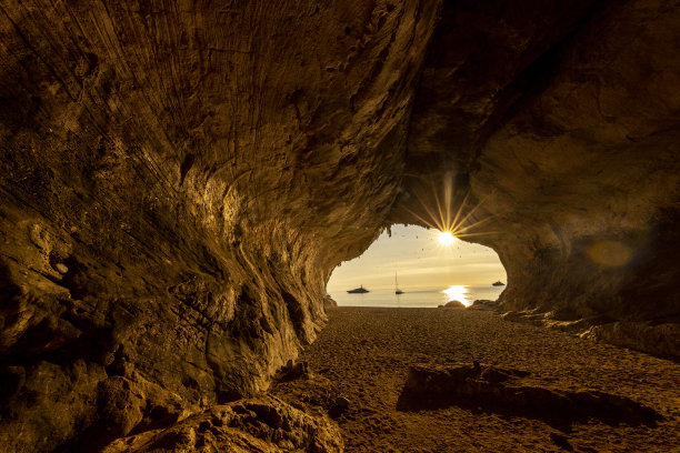 意大利撒丁岛，Cala Luna岩洞，夕阳西下，背景是帆船。图片下载
