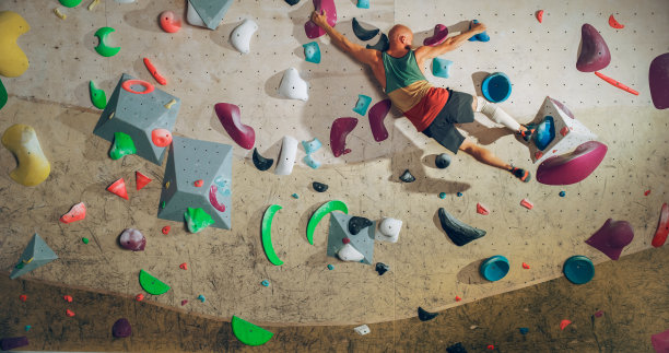 强壮的有经验的攀岩者在健身房独自攀爬抱石墙。男子在室内健身设施锻炼，为健康的生活方式训练做极限运动。射门。图片下载