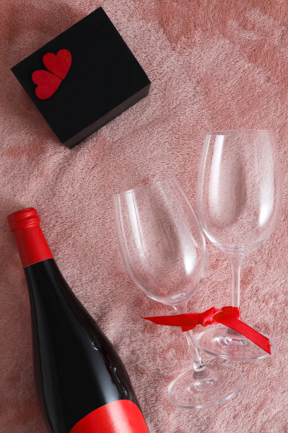 情人节贺卡葡萄酒，酒杯，黑色礼盒，红丝带和两颗红色的心在粉红色的皮毛背景。图片下载