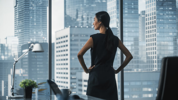 成功的女商人在时尚的服装看着窗外的大城市在市中心地区。从事金融项目的自信女性首席执行官。市场部经理。图片下载