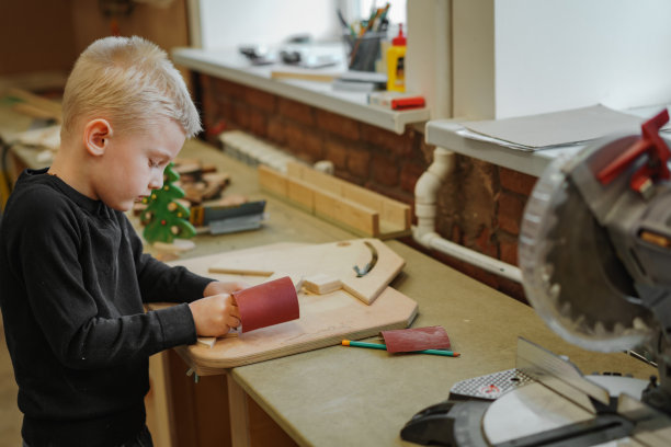 可爱的白人学龄前男孩在细木工课上啃木圣诞树。图片下载
