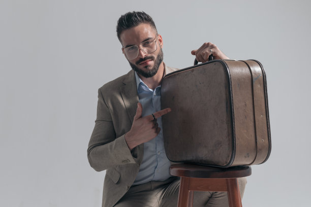 迷人的年轻商人指着手提箱微笑图片下载