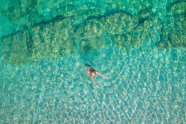 前,鸟瞰图。年轻漂亮的女子穿着白色比基尼在海水的沙滩上游泳。无人驾驶飞机,直升飞机的照片。暑假。从以上观点。图片下载
