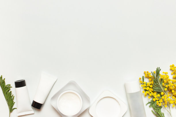 白色化妆品瓶子容器与黄色的含羞草花在光背景顶视图平躺。化妆品SPA品牌模拟，天然有机美容产品概念，极简主义化妆品风格图片下载
