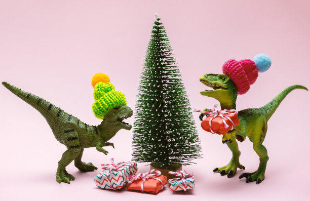 有趣的塑料玩具恐龙戴着针织帽子，有礼物盒和常青树在粉红色的背景上。图片下载