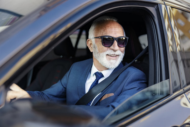一位年老的商人开着一辆汽车。一个快乐的高级商人坐在他的车里，他的手放在方向盘上，看着窗外。图片下载