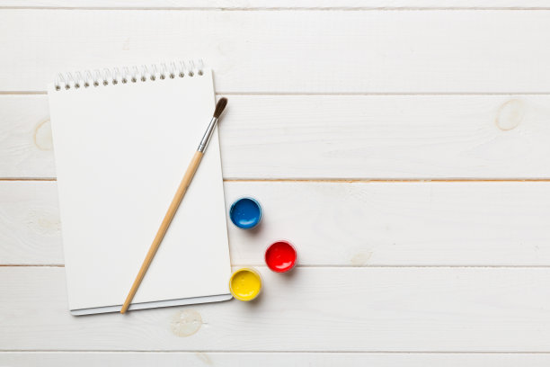 相册页和油漆，铅笔，画笔上的彩色背景。顶部视图与空的空间。工作场所的创造力。家庭教学概念图图片下载