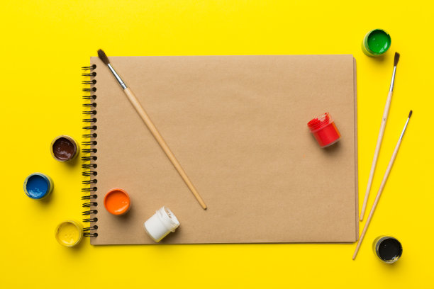 相册页和油漆，铅笔，画笔上的彩色背景。顶部视图与空的空间。工作场所的创造力。家庭教学概念图图片下载