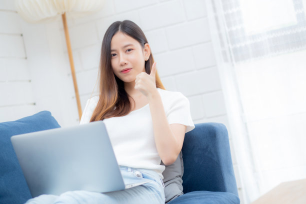 年轻的亚洲商业女性微笑着在家里用笔记本电脑上网，在客厅的沙发上上网，自由职业女孩用笔记本电脑在沙发上舒适，新常态，生活方式的概念。图片下载