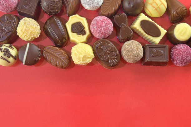 巧克力果仁糖。红色背景上的巧克力糖果。巧克力框架顶视图。巧克力果仁背景与文本复制空间。不同糖果的边界图片下载