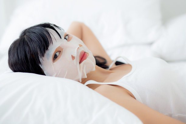 美丽年轻的亚洲妇女与床单面膜和睡在床上的卧室，美丽的女孩应用化妆品和皮肤护理面部皱纹，皮肤护理治疗，健康和健康。图片下载
