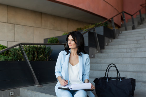 年轻漂亮的女商人在办公中心附近的楼梯上用笔记本电脑和文件工作，打电话图片下载