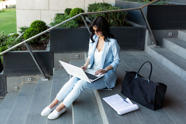 年轻漂亮的女商人在办公中心附近的楼梯上用笔记本电脑和文件工作，打电话图片下载