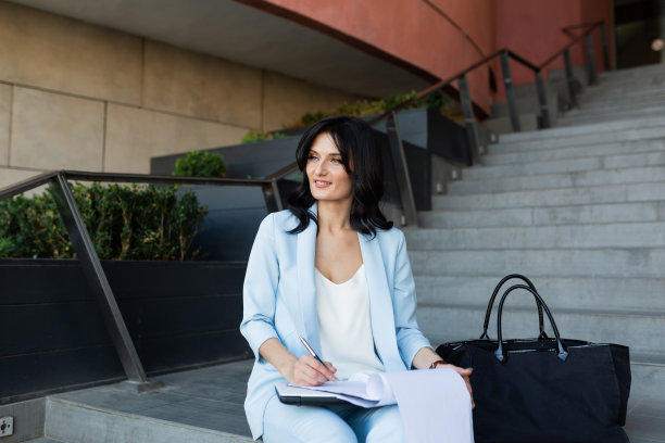 年轻漂亮的女商人在办公中心附近的楼梯上用笔记本电脑和文件工作，打电话图片下载