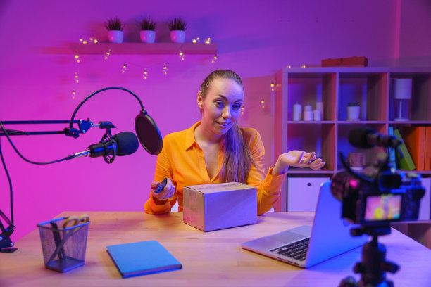 一个拍摄视频博客的后台，一个可爱的女博主，金发扎着马尾辫，穿着黄色衬衫，打开摄像机拍摄的一个盒子，我们看到了前景图片下载