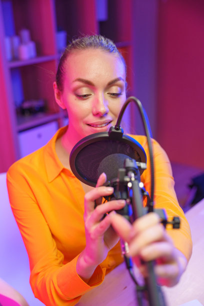 一个美丽的金发电台DJ在录音室里调整她的录音麦克风，我们看到她在专业灯光下腰部以上图片下载