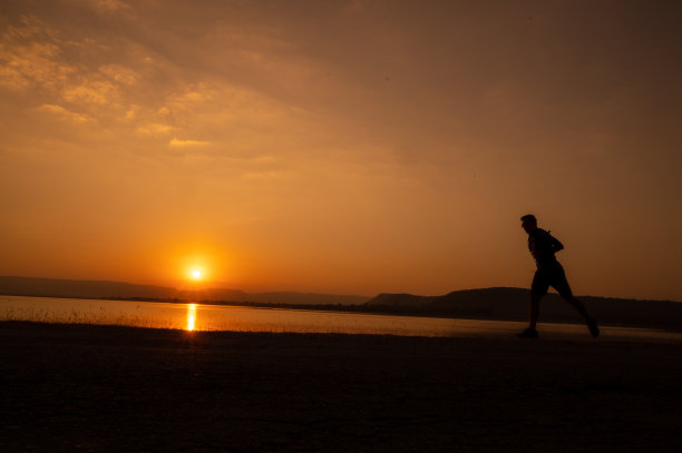 一个男人跑着剪影日落在湖和山图片下载