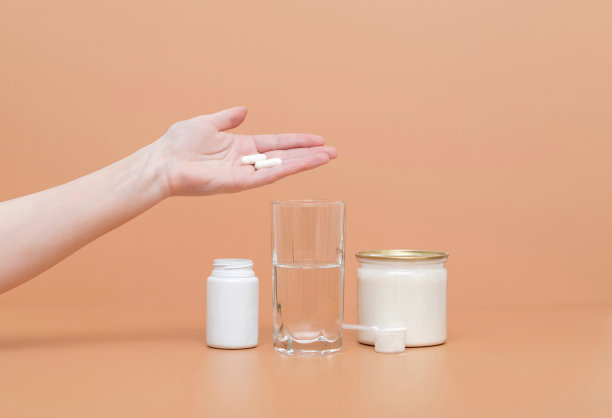 一只手在米色背景上拿着胶原蛋白药片。水解胶原蛋白粉在一个罐子和一杯水。健康生活方式的概念。图片下载