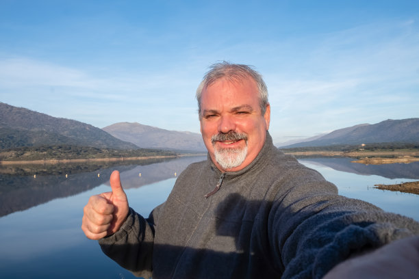 成熟的徒步旅行者在湖边的山顶上自拍。图片下载