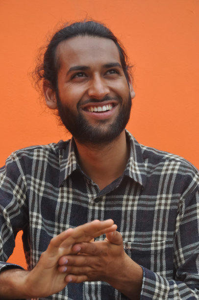 一个留着胡子的年轻人侧目微笑，在橙色的墙壁背景下摆姿势图片下载