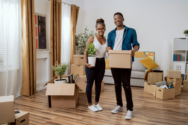 新婚夫妇搬进新家，他们把装了东西的纸板箱搬进客厅，女人布置好装饰品，手里拿着花盆，他们先一起装饰家图片下载