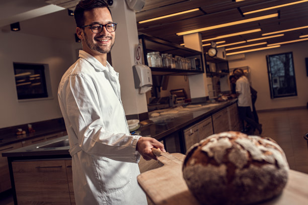 男性面包师在现代制造业中烘焙面包。图片下载