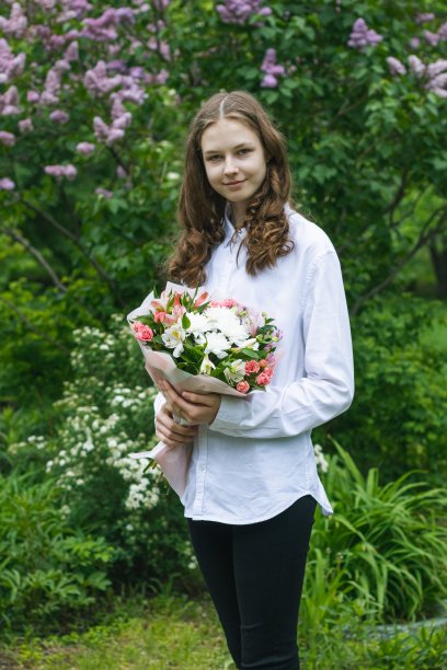 年轻美丽的女孩，肖像在花园的背景紫丁香。一个穿着白色上衣的女孩手里拿着一束美丽的花。图片下载