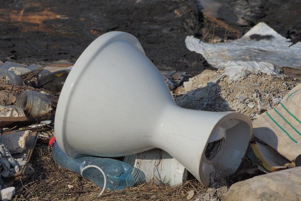 一个旧的白色陶瓷马桶躺在一堆垃圾中图片下载