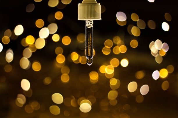 透明的血清移液器，滴在深色背景上，带有金色光线模糊和散景。化妆品问候的概念。极简主义风格和关闭。图片下载