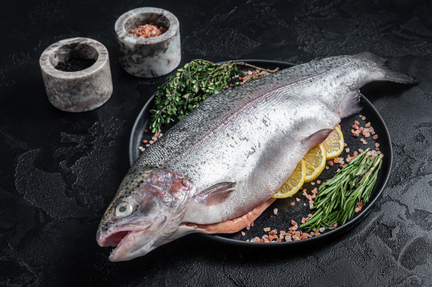 生海鳟鱼，新鲜的鱼和香草放在盘子里。黑色背景。俯视图图片下载