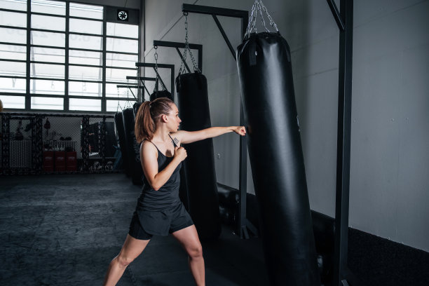 性感女孩在健身房里从事拳击训练。在黑暗的背景下，拳击女子拿着拳击袋摆姿势。在健身房用拳击包进行高强度锻炼。图片下载