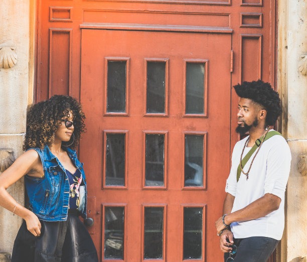 一对很酷的年轻黑人夫妇在一幢砖红色大门的城市建筑前闲逛图片下载