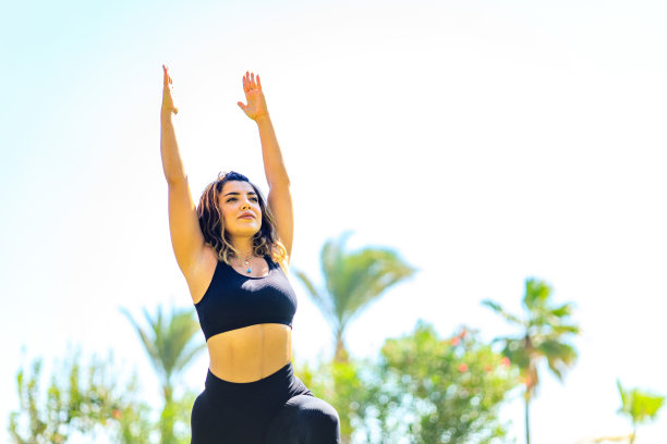 和谐的女人，脖子上戴着黄金首饰和耳环，在海滩附近的绿色背景上做瑜伽课图片下载