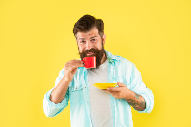 早上，一名穿着衬衫、满脸胡须的男子喝着黄色背景的咖啡图片下载